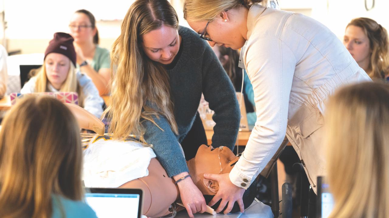 A faculty member guides a nursing student through a procedure on a dummy